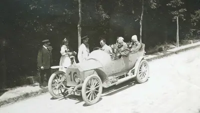 Robert Bosch, a woman and a man standing at the side of the road next to a racing car occupied by four racing drivers.
