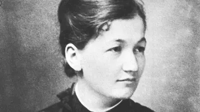 Portrait of a young woman with her hair tied up and wearing a blouse with the buttons done up to the top.