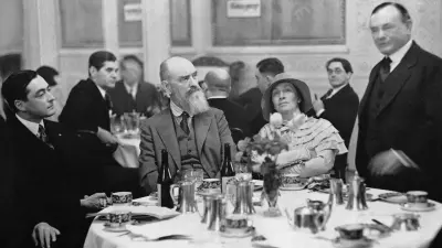 Robert Bosch, a man and a woman sitting at a table, a man standing next to them and giving a speech in a public room.