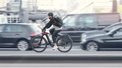 Man wearing a helmet cycles past a queue of cars.