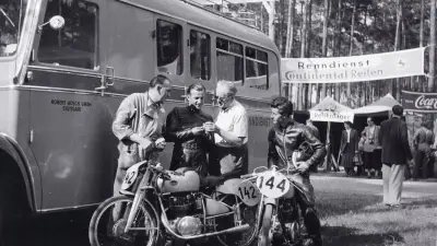 Four men with a motorcycle standing in front of a bus