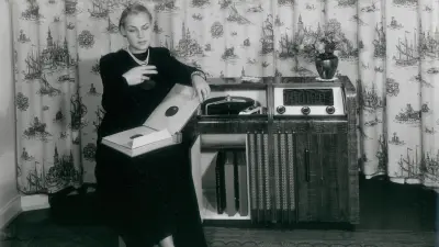 Eine Frau sitzt neben einem Radioapparat.