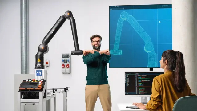 Two people are in a lab — one at a laptop, the other between a robot and its digital twin.