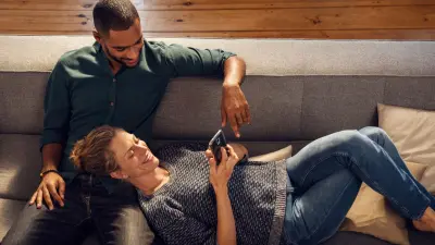 Paar liegt auf der Couch und schaut auf ein Handy