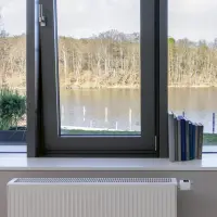 Ein Heizkörper mit einem intelligenten Thermostat vor einem Fenster mit Blick auf einen See.