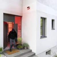 Ein Einbrecher rennt aus einem Haus, aus dem ein roter Lichtschein dringt.