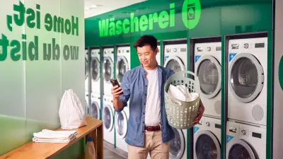 A man is standing in front of washing machines while holding a smartphone in his hand.