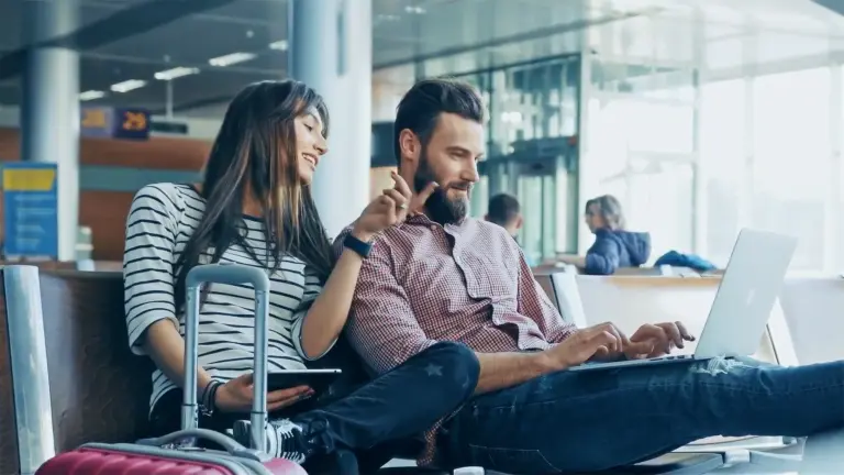 Two people sitting in an airport lounge using a laptop and a tablet.