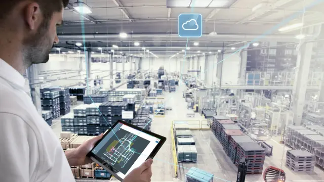 A man with a tablet in front of a connected factory hall.
