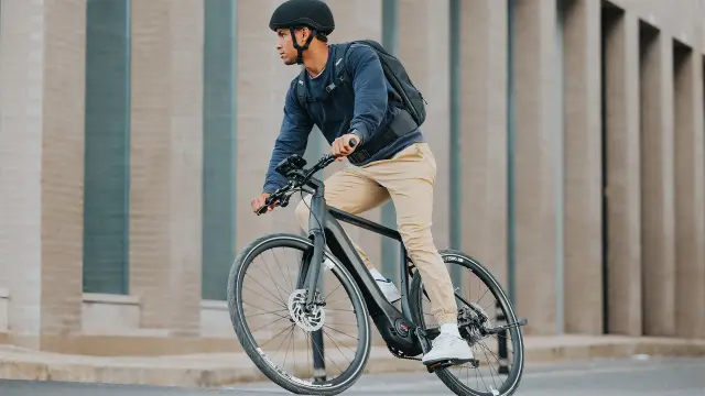 A man riding an eBike around a bend in front of a building in the city.