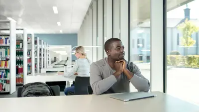 Young man sitting at a table in a library.