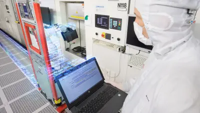 Technician in cleanroom suit working with semiconductor manufacturing equipment and laptop displaying data analysis, representing Bosch's embedded deep learning applications in high-tech production environments and AIoT systems.