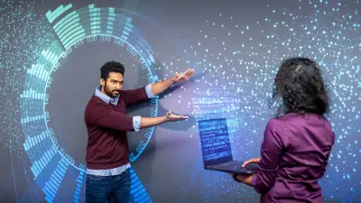 Two researchers collaborating with interactive holographic data visualization and AI interfaces, with one person gesturing toward floating digital displays while the other works on a laptop, representing Bosch's deep learning and explainable AI research.