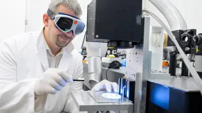 Scientist in white lab coat and protective eyewear working with precision laboratory equipment and microscopy systems, representing AI-enhanced research and development in Bosch engineering and product innovation.