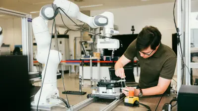 Worker in green shirt operating alongside white industrial robotic arm in modern manufacturing facility, demonstrating human-robot collaboration and AI-driven automation in Bosch production environments.