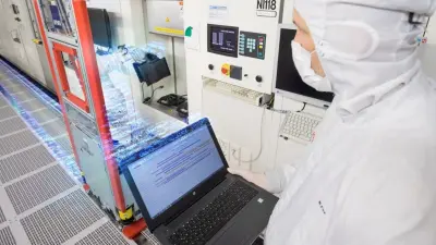 Artificial intelligence in manufacturing at the Bosch Automotive Electronics wafer factory in Reutlingen, Germany. ALT-Tag: Bosch employee at Bosch wafer factory in Reutlingen walks through the plant in a cleanroom suit and carries a laptop with data in his hand.