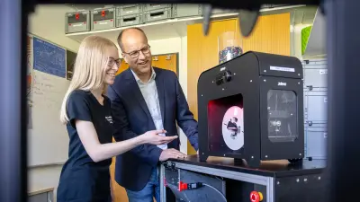 3D printer in operation in a lab environment with filament spool and control panel visible