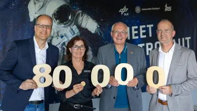 Group holds large wooden numbers forming 80,000 in front of a space-themed backdrop
