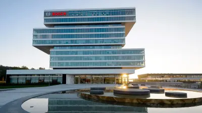 The picture shows the main building of Bosch Research in Renningen - a futuristic, glazed high-rise in the sunrise with a fountain in front of it.