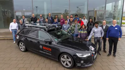Gruppenbild der Kooperationsmitglieder bei einem Treffen im Bosch Research Hauptquartier in Renningen, Deutschland vor dem Eingangsgebäude. Ein automatisiertes Fahrzeug steht vor den Kooperationsmitgliedern.