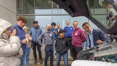Die Projektmitglieder blicken in den Kofferraum eines automatisierten Fahrzeugs. Diverse Kabel und Schläuche ragen heraus.