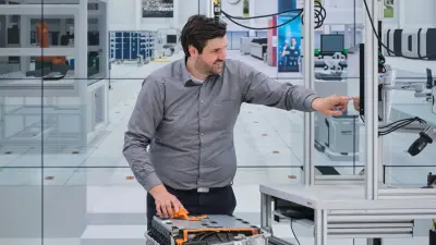 Bosch research expert Matthias Kayser in a modern model-making hall (ARENA2036 in Stuttgart). He points to a screen that, with the help of Bosch's DeepInspect system, shows him whether his component has been installed correctly or not.