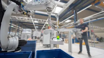 The picture shows Bosch Research’s and Bosch Rexroth’s Smart Item Picking system in an industrial environment. The robotic arm picks up an object from the conveyor belt.