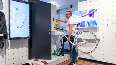 : Bosch Research Mitarbeiter steht im Renninger Smart Life Lab mit einem Fahrrad in der Hand. An einen großen Screen lässt er sich seinen Radweg anzeigen.