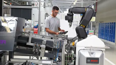 The picture shows the Bosch APAS automatic production assistant together with an associate during a work process.