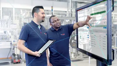 Zwei Bosch-Mitarbeiter vor einem interaktiven Screen in einer Produktionshalle.