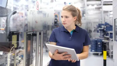Eine Frau mit einem Tablet in der Hand in einer Produktionshalle.