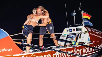Two people embrace on a rowing boat at night, celebrating the arrival.