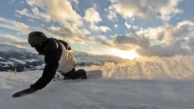 A snowboarder turning hard into a curve, touching the snow with his hand.