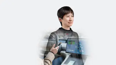 Person seated in a vehicle with view of steering wheel and digital driver assistance display.