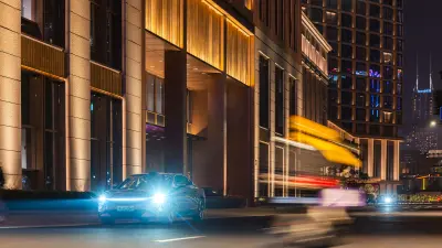 Car driving at night past illuminated modern buildings