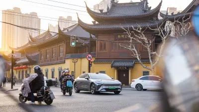 Car driving through traffic with scooters and pedestrians nearby