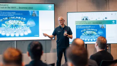 Martin Thomas, a middle-aged man with glasses and grey hair, wearing a dark Bosch polo shirt, presents to an audience. Large screens behind him display diagrams and text.