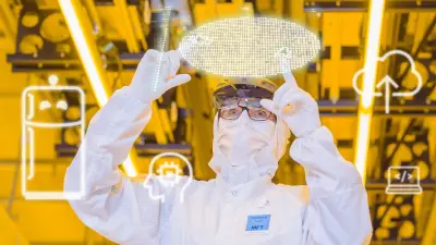 A person in a white protective suit stands in a yellow-lit clean room and points with both hands to a virtually superimposed wafer.