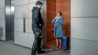 Mechanic assisting a grateful woman with her luggage inside an elevator.