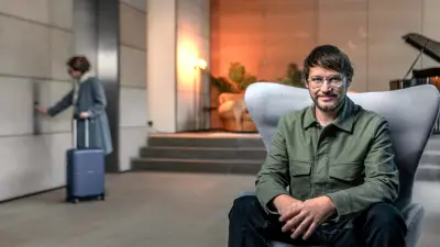 Man relaxing in hotel lobby as another guest calls for elevator.