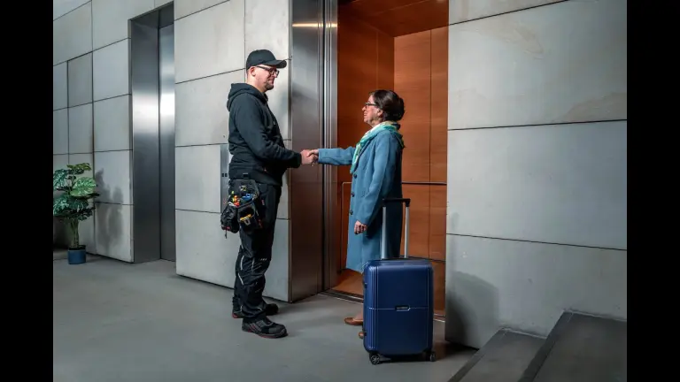 Maintenance worker assisting a hotel guest with luggage by elevator.