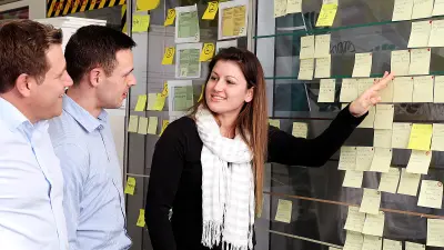 Three members of the Ixo team are standing in front of the sprint board, which has a lot of notes, and discuss tasks