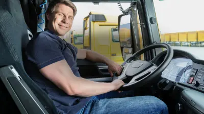 Lkw-Fahrer sitzt im Fahrerhaus seines Lkw am Steuer und lacht