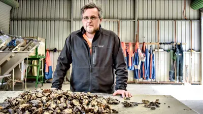 Oyster farmer Justin Goc standing in a storehouse next to a pile of fresh oysters.