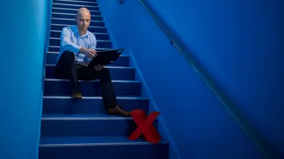 The picture shows Sebastian Krauskopf sitting on a blue staircase with a laptop in his hand.