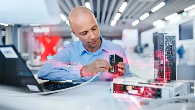 Sebastian Krauskopf sitzt an einem Tisch und verbindet eine Bauform der ctrlX AUTOMATION mit einem Computer. Im Vordergrund sind weitere Bauformen zu sehen.