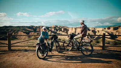 Two people with bicycles stand by a wooden railing overlooking eroded rock formations.