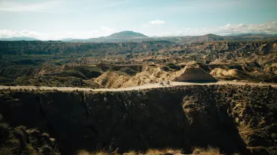 Two cyclists on a gravel road in the middle of a wide mountainous and hilly landscape.