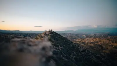 Mountain landscape at dusk with a small group visible on a distant ridge.