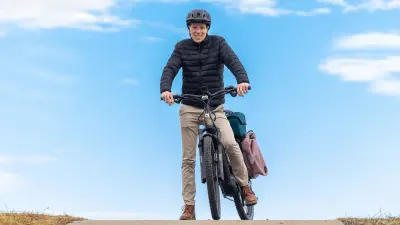 Person standing outdoors with a bicycle under a bright blue sky.